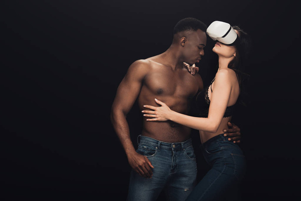 african american man hugging sexy woman in virtual reality headset isolated on black with copy space - Photo, Image