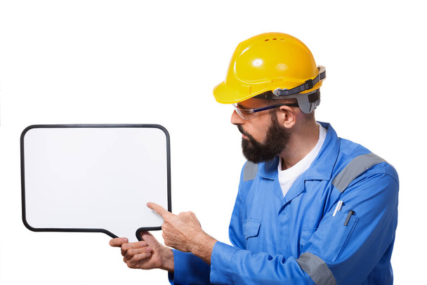 Bearded worker in protective construction helmet pointing to the white chalk board with copy space, isolated over white background - 写真・画像