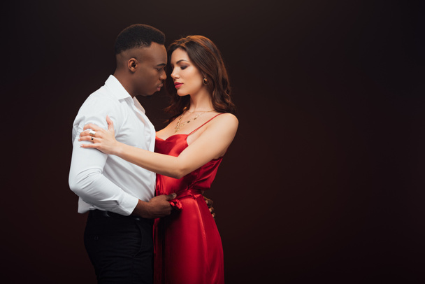 beautiful interracial couple in formal wear embracing isolated on black with copy space - Photo, Image