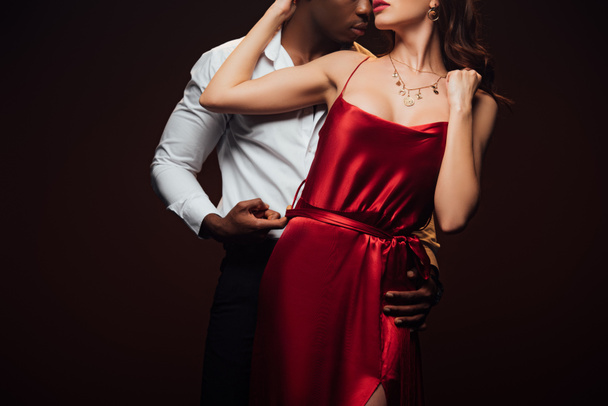 partial view of african american man embracing woman in red dress isolated on black - Photo, Image