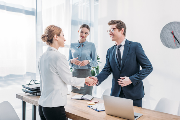 cheerful recruiter shaking hands with woman near colleague in office - Photo, Image