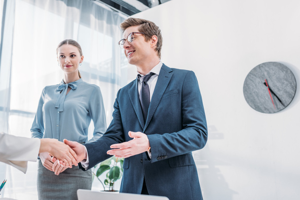 low angle view of cheerful recruiter shaking hands with woman near attractive colleague in office - Foto, Imagem