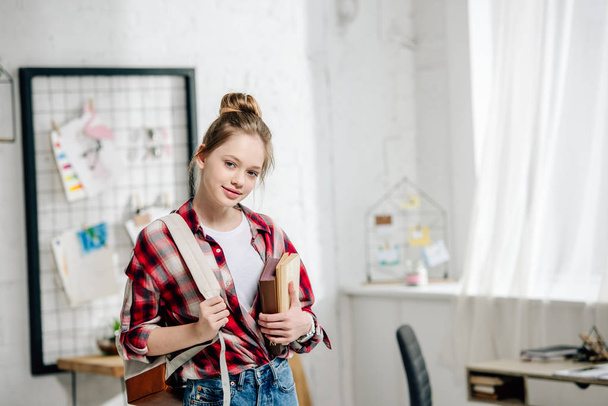 Teenage schoolgirl in checkered shirt with backpack holding books - Foto, Imagen