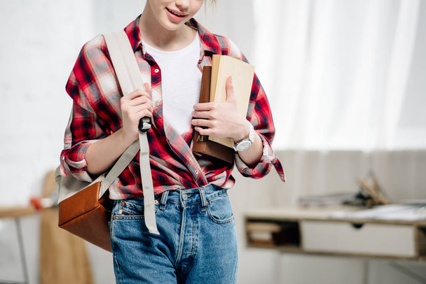 Cropped view of teenage schoolgirl in checkered shirt with backpack holding books - Φωτογραφία, εικόνα
