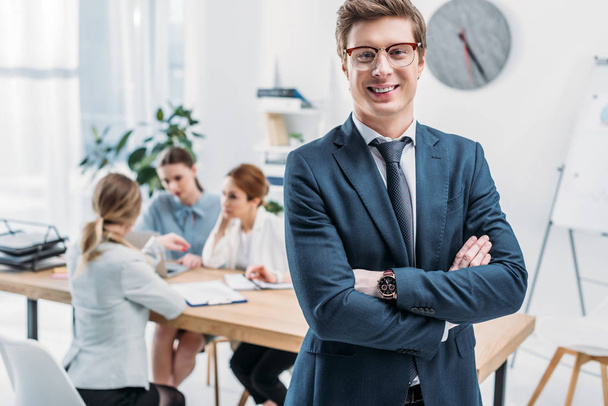 selective focus of cheerful recruiter in glasses standing with crossed arms near coworkers  - Photo, Image