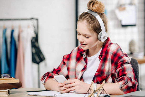 Joyful teenage kid in red checkered shirt listening music in headphones - Photo, Image