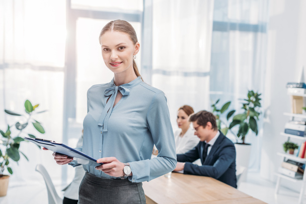 selective focus of cheerful woman standing with clipboard near coworkers  - Photo, Image