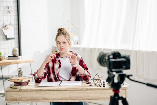 Teenage blogger sitting at desk in front of video camera and making video - Fotografie, Obrázek