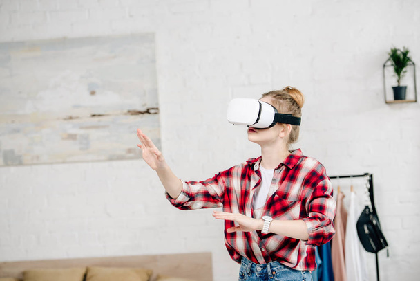Teenager in red checkered shirt and vr headset gesturing at home - Foto, Imagem