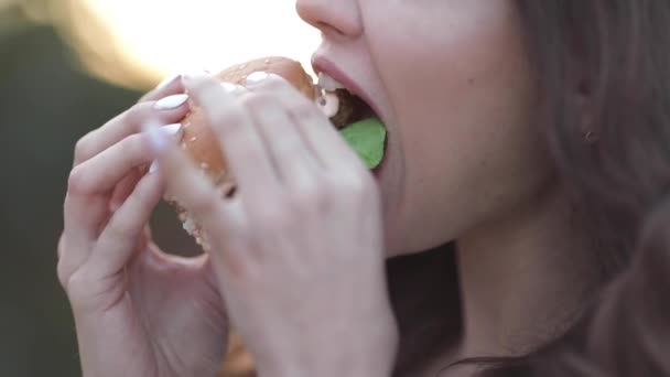 Teen girl in stylish sunglasses with bright lips enjoying delicious burger. - Imágenes, Vídeo