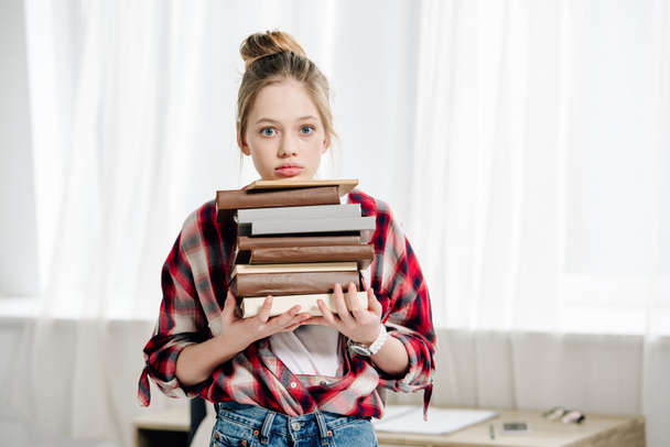 Adolescente con camisa a cuadros roja sosteniendo libros en casa
 - Foto, Imagen