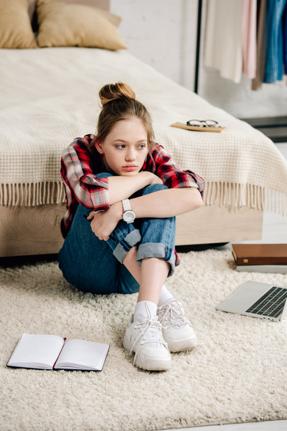 Znuděný teenager v kostené košili, sedící u postele a objímající kolena - Fotografie, Obrázek