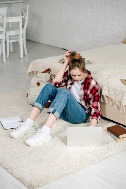 Tiener met laptop en boeken zittend op tapijt en doen huiswerk - Foto, afbeelding