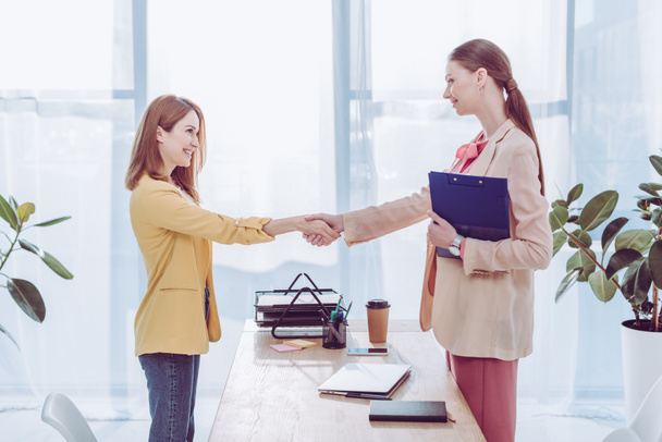 felice reclutatore tenendo appunti e stringendo la mano con la donna in ufficio moderno
  - Foto, immagini