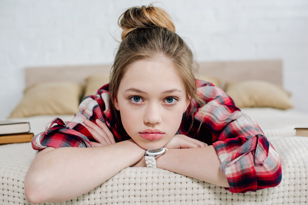 Front view of teenager kid in wristwatch lying on bed and looking at camera - Photo, Image