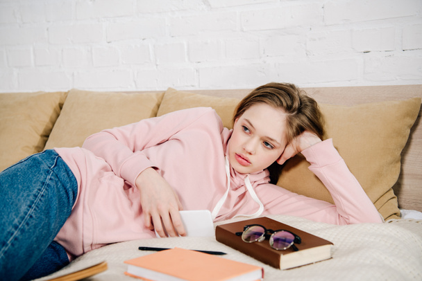 Fáradt tizenéves gyerek feküdt ágyon könyvek és okostelefon - Fotó, kép