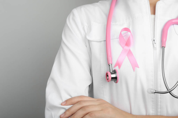 Doctor with pink ribbon and stethoscope on grey background, space for text. Breast cancer awareness - Foto, Imagem