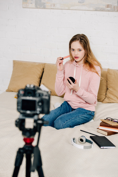 Blogueur adolescent assis sur le lit et faisant du maquillage devant la caméra vidéo
 - Photo, image