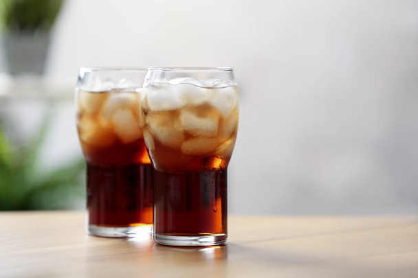 Glasses of cola with ice on table against blurred background, space for text - Photo, image