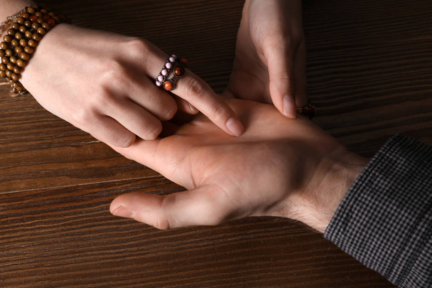 Chiromancer reading lines on man's palm at table, closeup - Zdjęcie, obraz