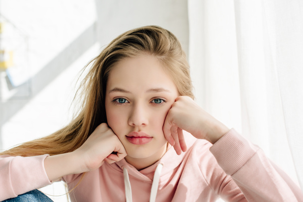 Front view of bored teenage kid in pink hoodie propping face with hands and looking at camera - Foto, immagini