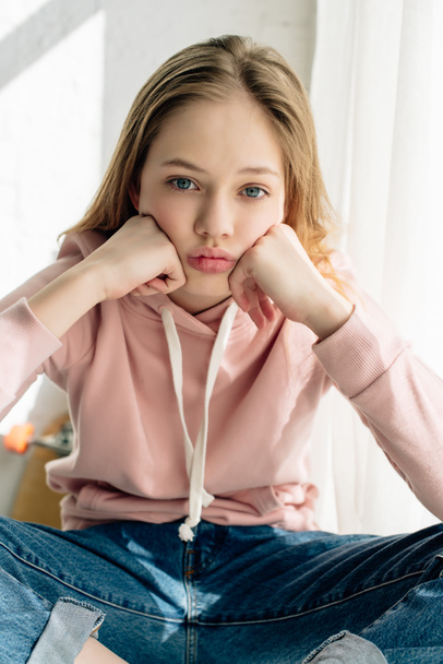Front view of bored teenage kid in pink hoodie propping face with hands and looking at camera - Fotó, kép