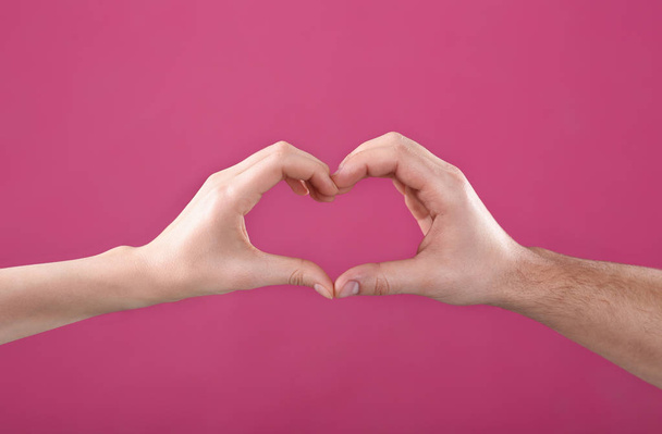 Чоловік і жінка роблять серце своїми руками на кольоровому фоні, крупним планом
 - Фото, зображення