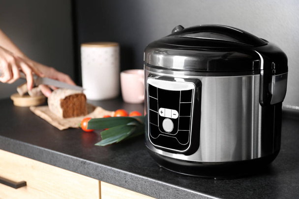 Modern multi cooker and woman slicing bread on table in kitchen, space for text - Foto, immagini