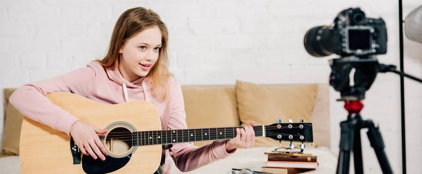 Panoraamakuva teini bloggaaja pelaa akustista kitaraa videokameran edessä
 - Valokuva, kuva