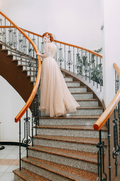 The bride is in an expensive hotel on the stairs. Wedding photo shoot in a beautiful dress. - Фото, изображение