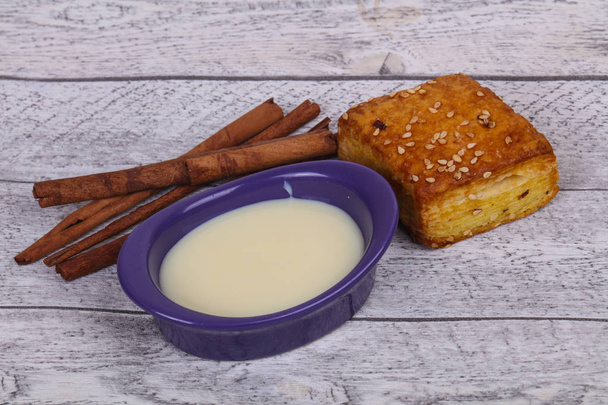 Condenced milk in the bowl with sinnamon sticks and pastry - Photo, Image