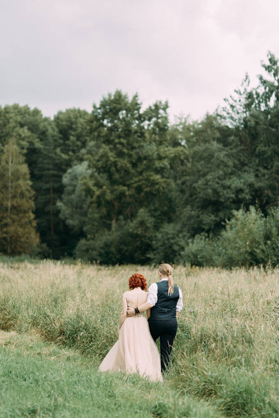 Wedding ceremony in nature in the field. Bride and groom walking on the grass. - Photo, image