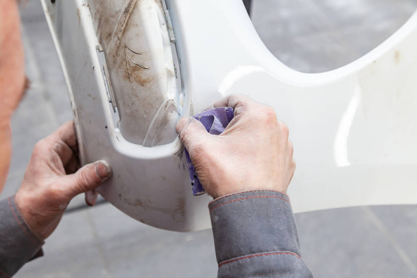 Мужчина готовит элемент кузова автомобиля к покраске после аварии
 - Фото, изображение