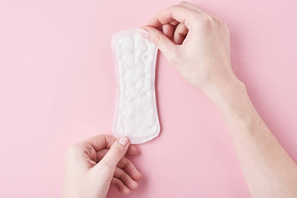 Woman hands hold sanitary pad on a pink background - Foto, Imagen