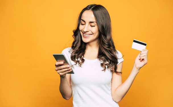 That was a breeze! A girl with a credit card in one hand and a mobile phone in other is showing her pleasant emotions and satisfaction because of using this devices. - Foto, Imagen