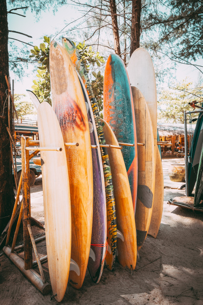 Conjunto de diferentes tablas de surf de colores en una pila disponible para alquilar en la playa. Tablas de surf verticales, efecto de tono de color vintage
. - Foto, Imagen