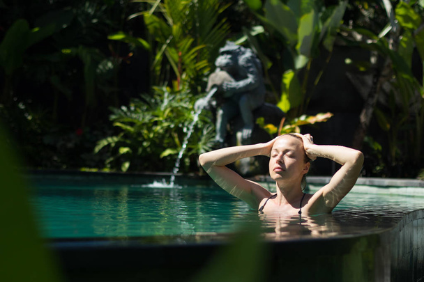 Sensual young woman relaxing in outdoor spa infinity swimming pool surrounded with lush tropical greenery of Ubud, Bali. - Photo, Image