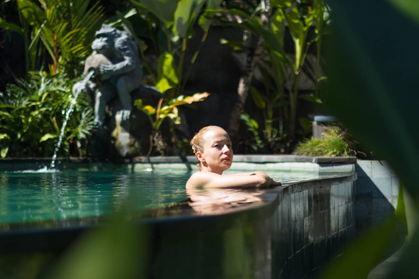 Érzéki fiatal nő pihentető szabadtéri spa végtelen medence körül buja trópusi növényzet Ubud, Bali. - Fotó, kép