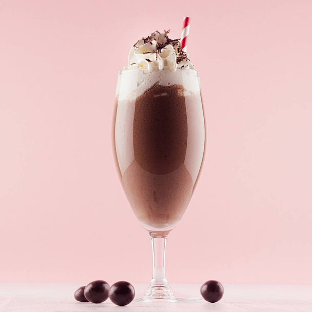 Chocolate milkshake with sweet whipped cream, straw and candies in modern stylish pink interior on white wooden table, square. - Photo, image