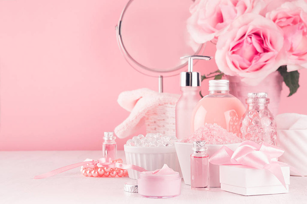 Gentle girlish dressing table with round mirror, flowers and cosmetics products - rose oil, bath salt, cream, perfume, cotton towel, bottle and bowl in white, pastel pink interior. - Zdjęcie, obraz
