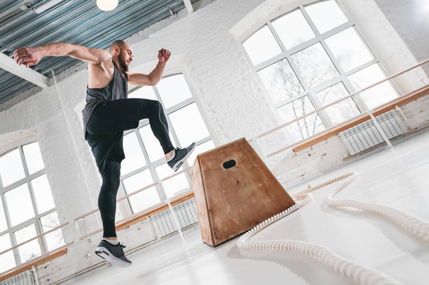 Strong fitness man doing jump exercises on box in gym. Fit athlete wearing sportswear and jumping over box in sport hall - Foto, Imagem