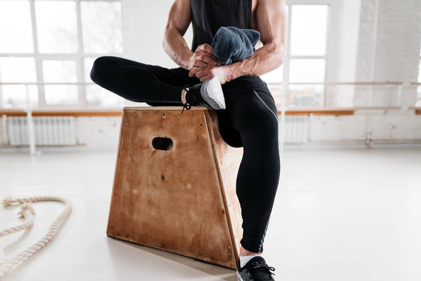 Close up view on strong male athlete resting on wooden box after cross intense in workout gym. Fit perspiring man sitting on box in fitness hall - Φωτογραφία, εικόνα