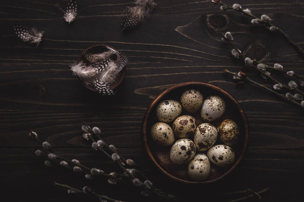 Organic quail eggs in wooden bowl and pussy willow branches on dark wooden background.  - Fotó, kép