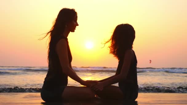 Mãe e filha estão sentadas juntas na praia de mãos dadas ao pôr do sol
 - Filmagem, Vídeo