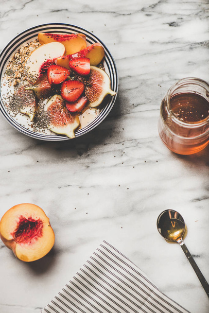 Healthy summer breakfast set. Flat-lay of Greek yogurt granola bowl with strawberry, figs, peach, chia seeds and honey over marble background, top view, copy space. Vegetarian, dieting food concept - Foto, afbeelding