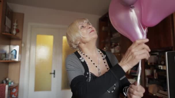 Χαριτωμένο γιαγιά γιορτάζει τα γενέθλιά της. Πολύχρωμα μπαλόνια κρατά στα χέρια της - Πλάνα, βίντεο