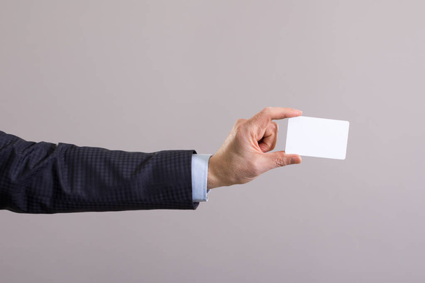 Mano de un hombre de negocios con una tarjeta en blanco sobre un fondo gris
. - Foto, imagen