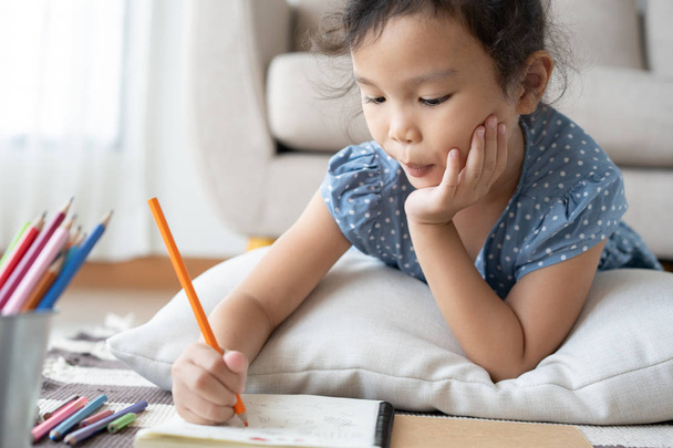 Cute little girl drawing homework and writing with pen on paper in her home - Photo, image