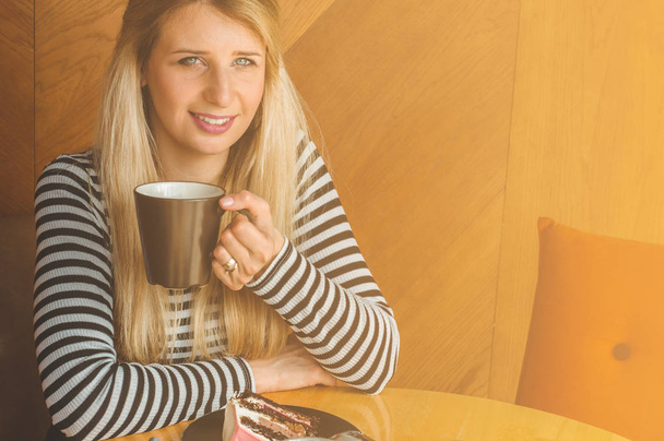 Όμορφο κορίτσι σε ένα καφέ απολαμβάνοντας ένα ζεστό τσάι. Hipster κορίτσι εκμετάλλευση ζεστό τσάι. Αναψυκτικό ποτό στην ηλιόλουστη μέρα - Φωτογραφία, εικόνα