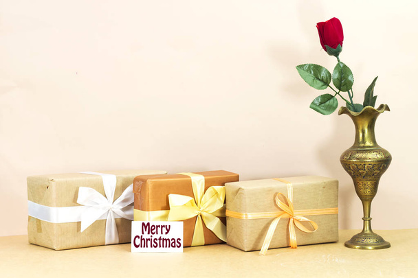 red rose flower in east gold antique brass vase, and boxes gifts with merry christmas card - Photo, Image